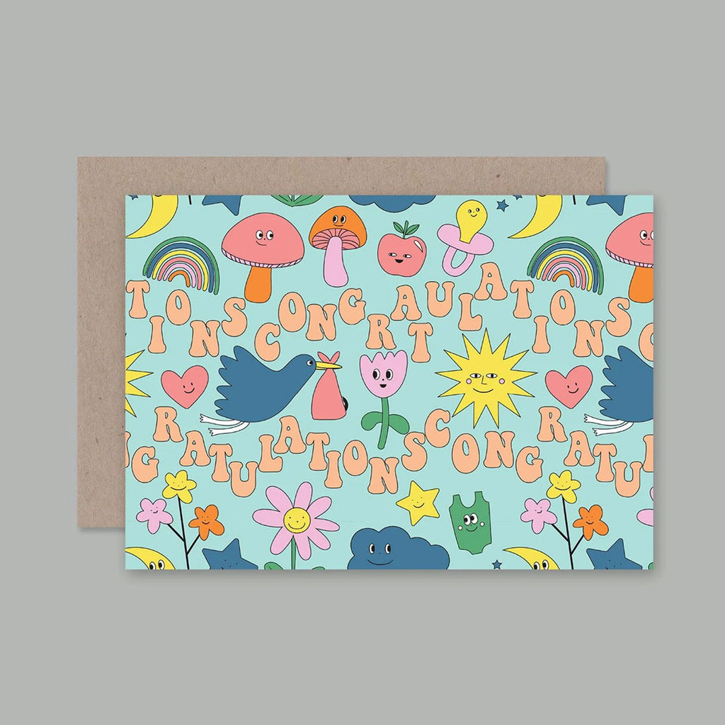 A greeting card with a playful multicolour cartoon pattern on a light blue background, shown with a brown kraft envelope behind it on a neutral grey background.