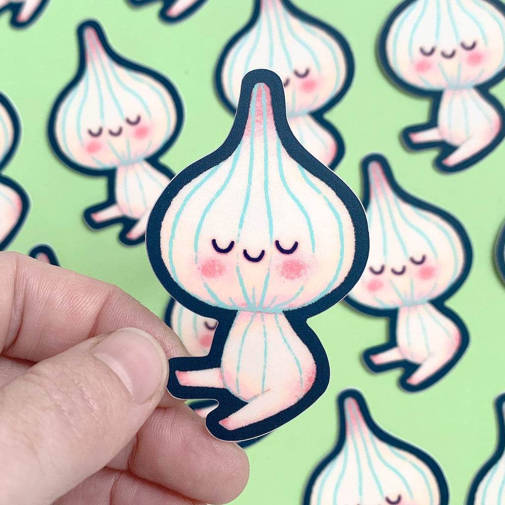 Hand holding a cute cartoon-style garlic character sticker with a pattern of similar stickers in the background.