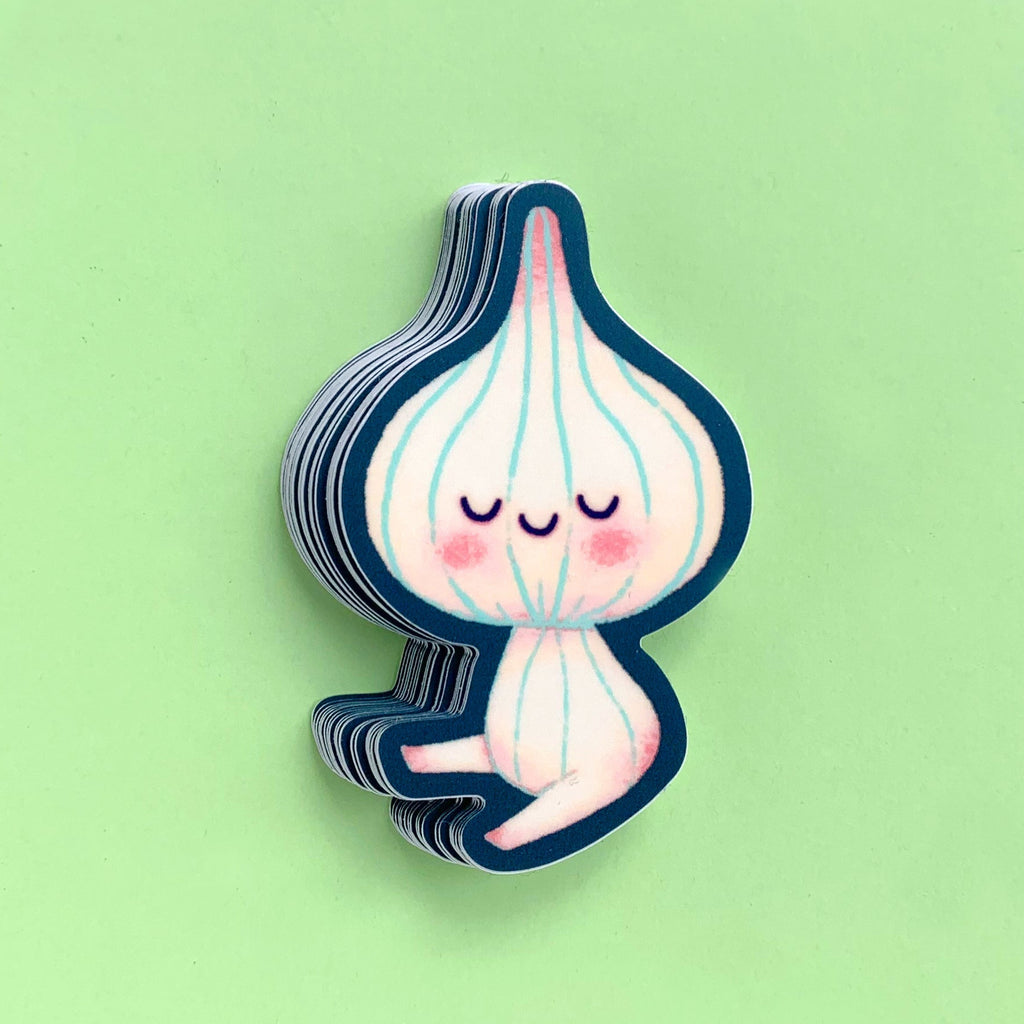 A stack of small die-cut stickers featuring a cute cartoon garlic bulb character with closed eyes, pink cheeks, and light blue vertical lines, shown on a solid light green background.