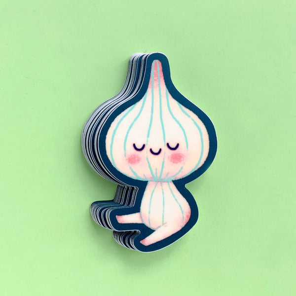 A stack of small die-cut stickers featuring a cute cartoon garlic bulb character with closed eyes, pink cheeks, and light blue vertical lines, shown on a solid light green background.