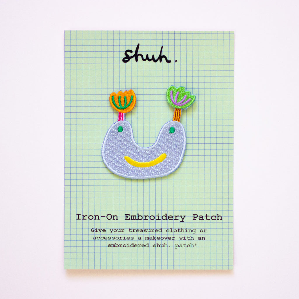 Iron-on embroidery patch with colorful design on a green checkered card