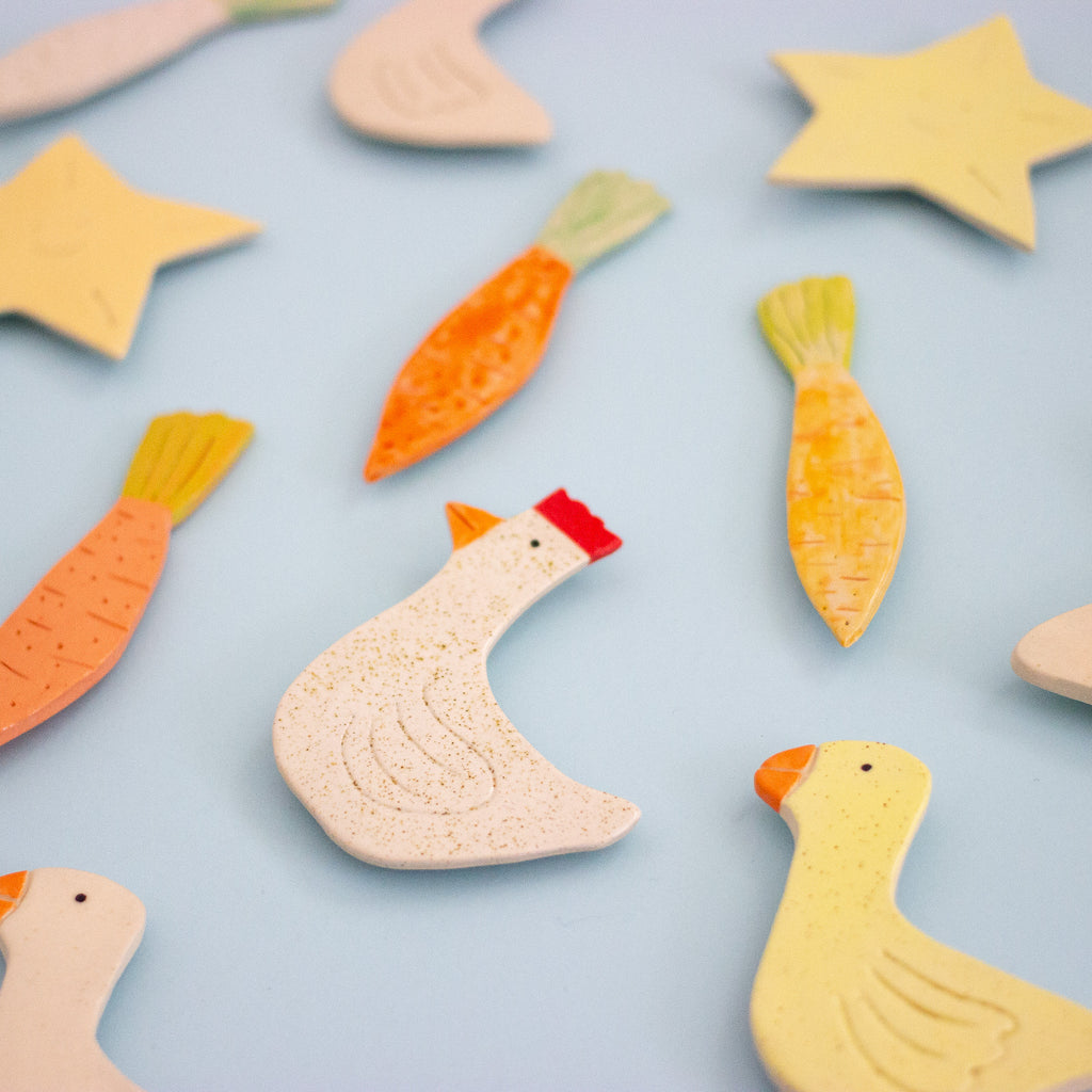 Colorful ceramic animal magnets including carrots and a duck on a light blue background