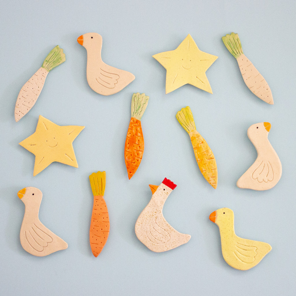 Set of colorful ceramic animal and vegetable-shaped magnets on a light blue background