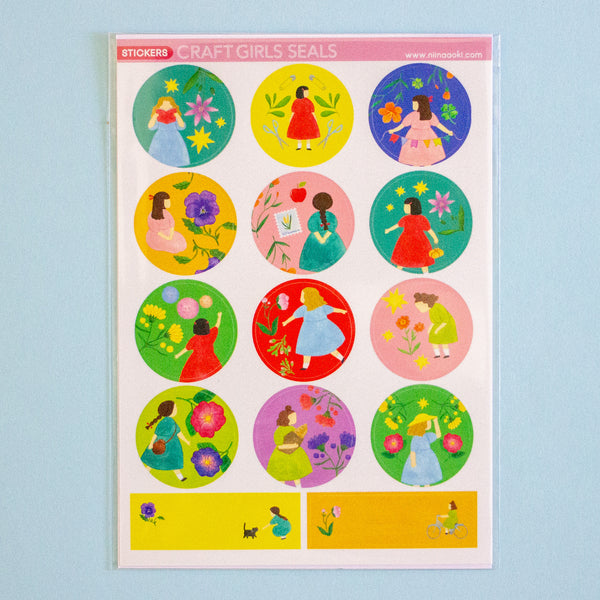 A sheet of circular stickers featuring colourful cartoon girls in dresses among flowers and plants, with a pink header reading 'STICKERS CRAFT GIRLS SEALS' on a light blue background.