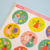 A close-up of a sticker sheet titled 'STICKERS CRAFT GIRLS SEALS' showing several colourful circular stickers with illustrated girls and flowers on a pale blue background.