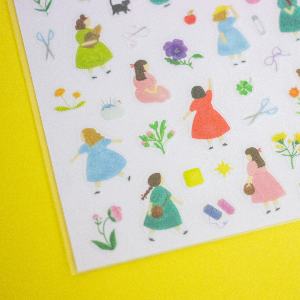 A sheet of colourful sticker illustrations featuring girls in dresses, flowers, and small accessories, photographed on a bright yellow background.