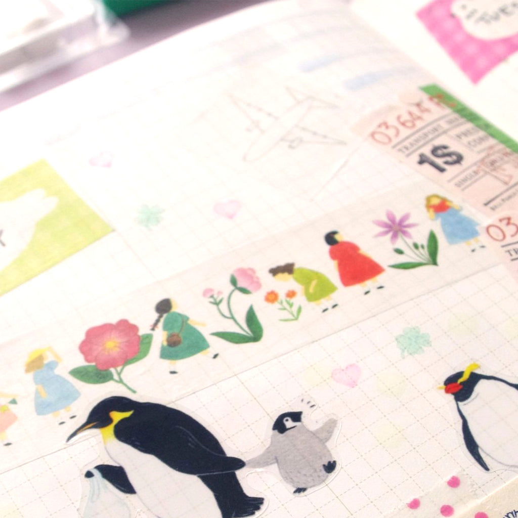 A close-up of a decorative planner or journaling strip with illustrated penguins, flowers, small figures, and pastel motifs on a white grid paper background.