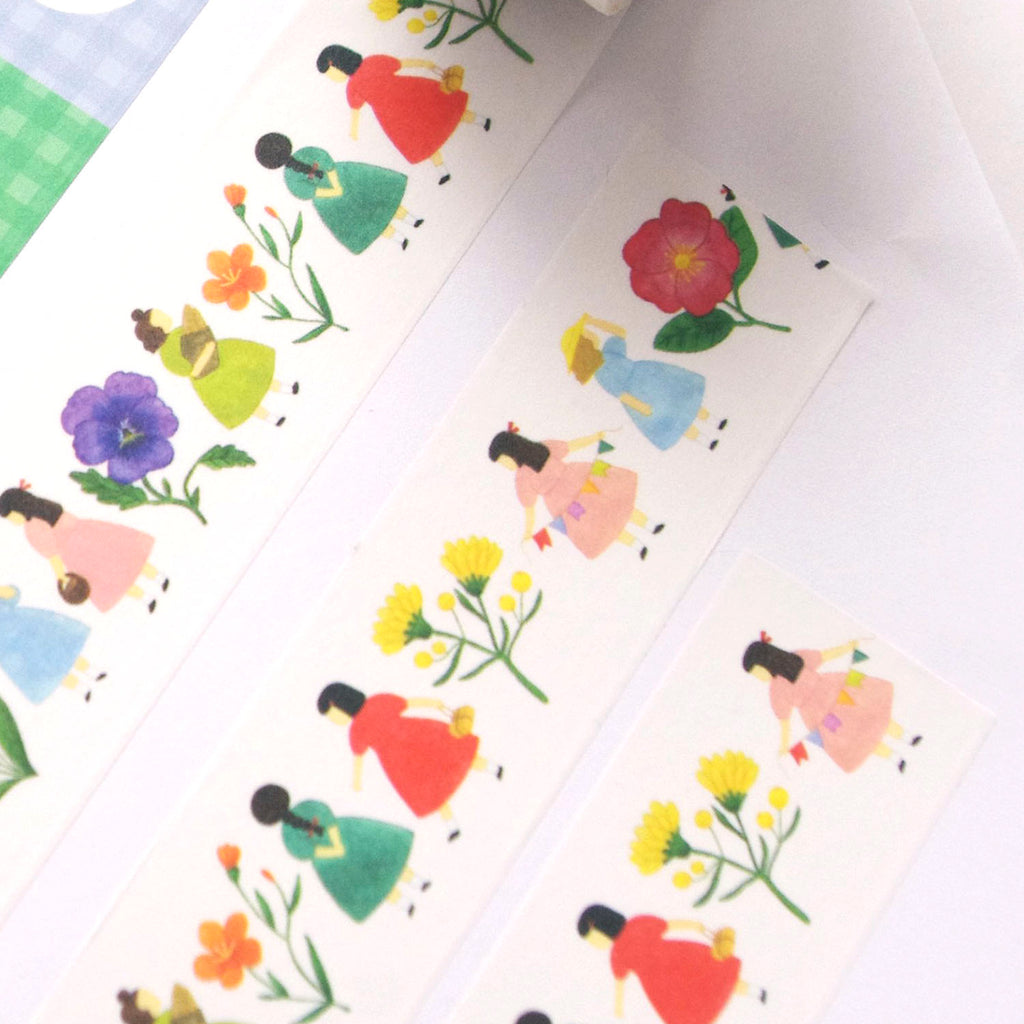 A close-up of decorative paper strips featuring a repeating illustration of girls in colourful dresses walking beside flowers, photographed on a white surface.