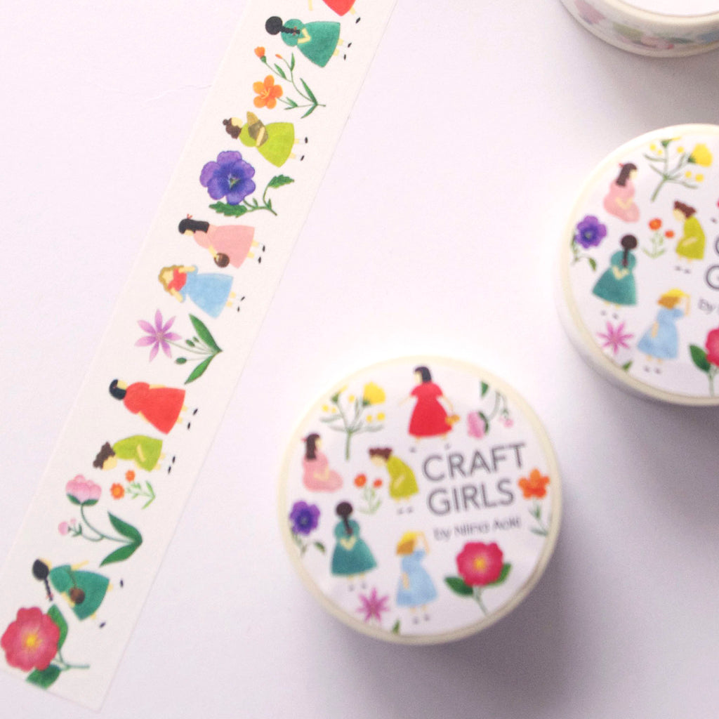 A close-up of decorative paper strips featuring a repeating illustration of girls in colourful dresses walking beside flowers, photographed on a white surface.