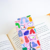 A pastel pink bookmark with colourful cartoon animal illustrations is tucked between open book pages.