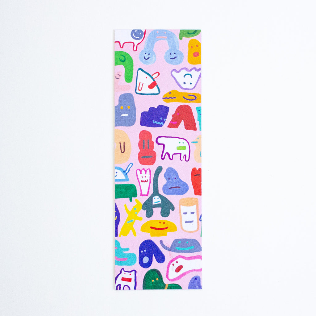 A tall, narrow rectangular bookmark with a light pink background covered in a colourful pattern of whimsical cartoon shapes and faces, shown against a plain white background.