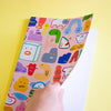 Front cover of the creatres a5 notebook. Pink background with varied characters and monsters from shuh.'s imagation. Also show's blank pages inside. 