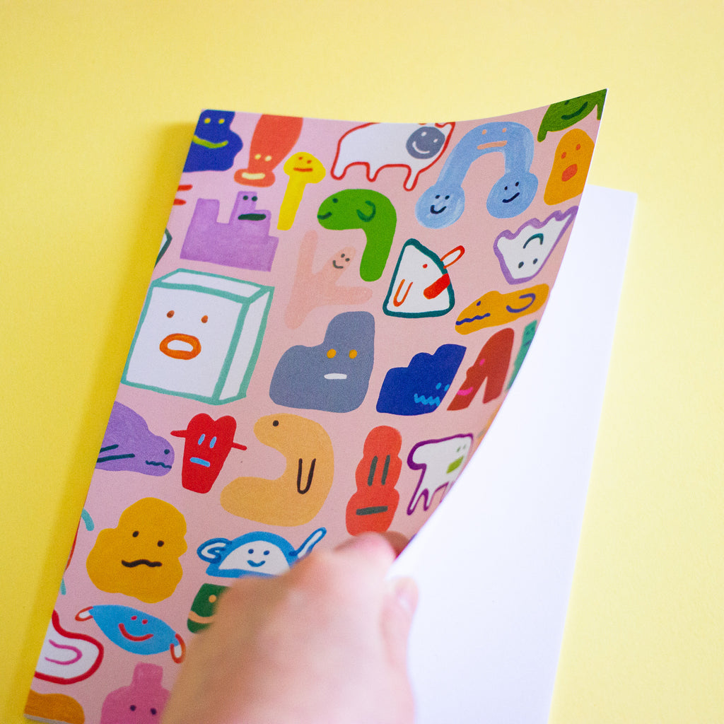 Front cover of the creatres a5 notebook. Pink background with varied characters and monsters from shuh.'s imagation. Also show's blank pages inside. 