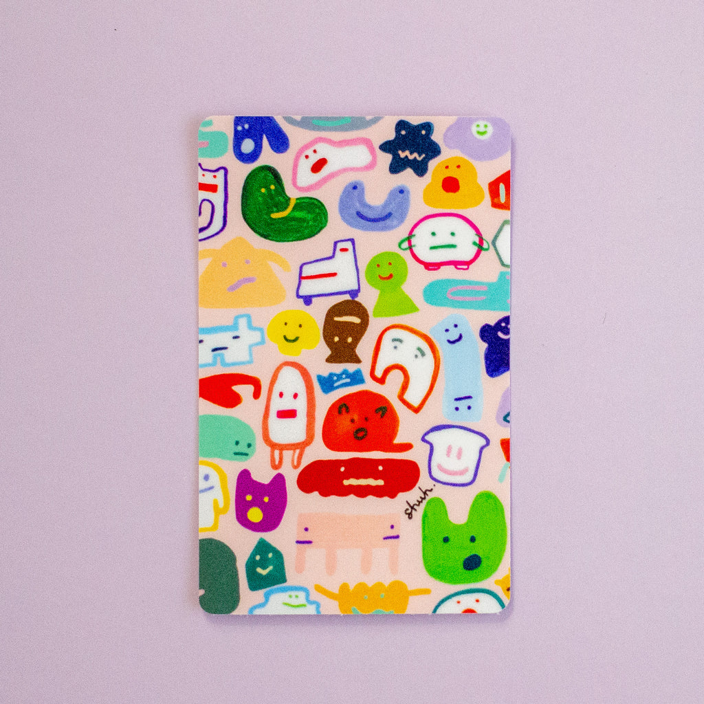 A vertical sticker featuring a colourful cartoon character pattern on a pale pink background, photographed against a solid lavender-purple backdrop.