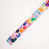 A close-up of a colourful washi tape, featuring whimsical cartoon characters and abstract shapes in pink, blue, green, yellow, purple, and orange on a white background.