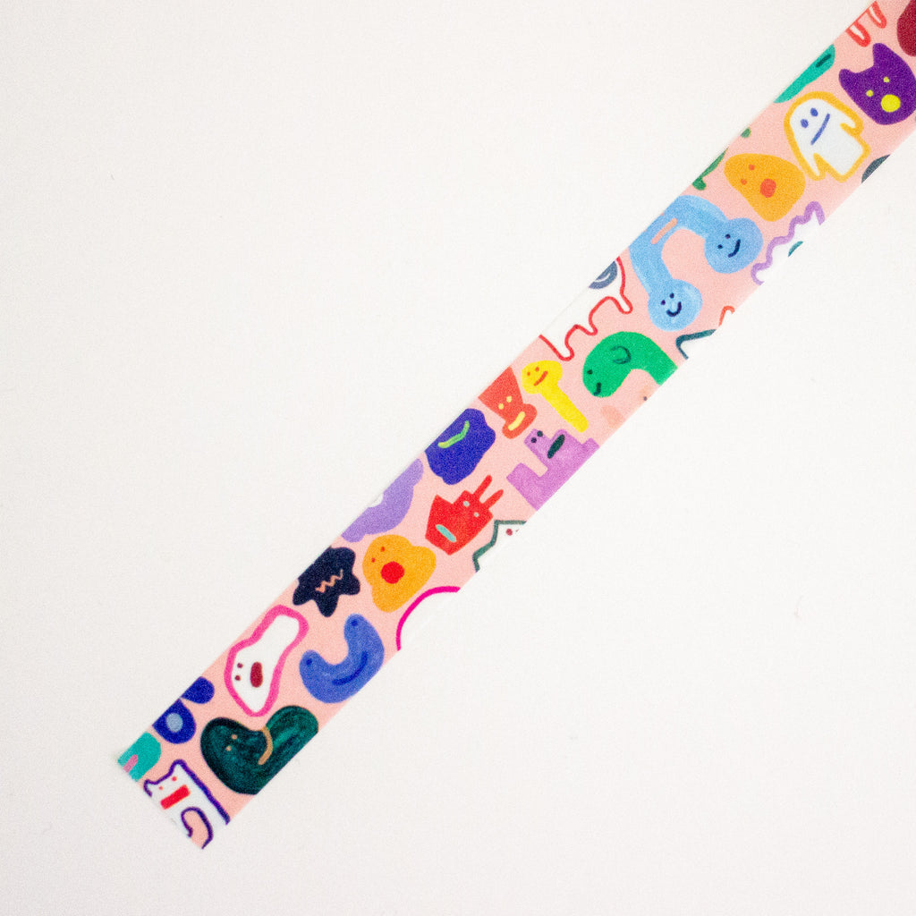 A close-up of a colourful washi tape, featuring whimsical cartoon characters and abstract shapes in pink, blue, green, yellow, purple, and orange on a white background.