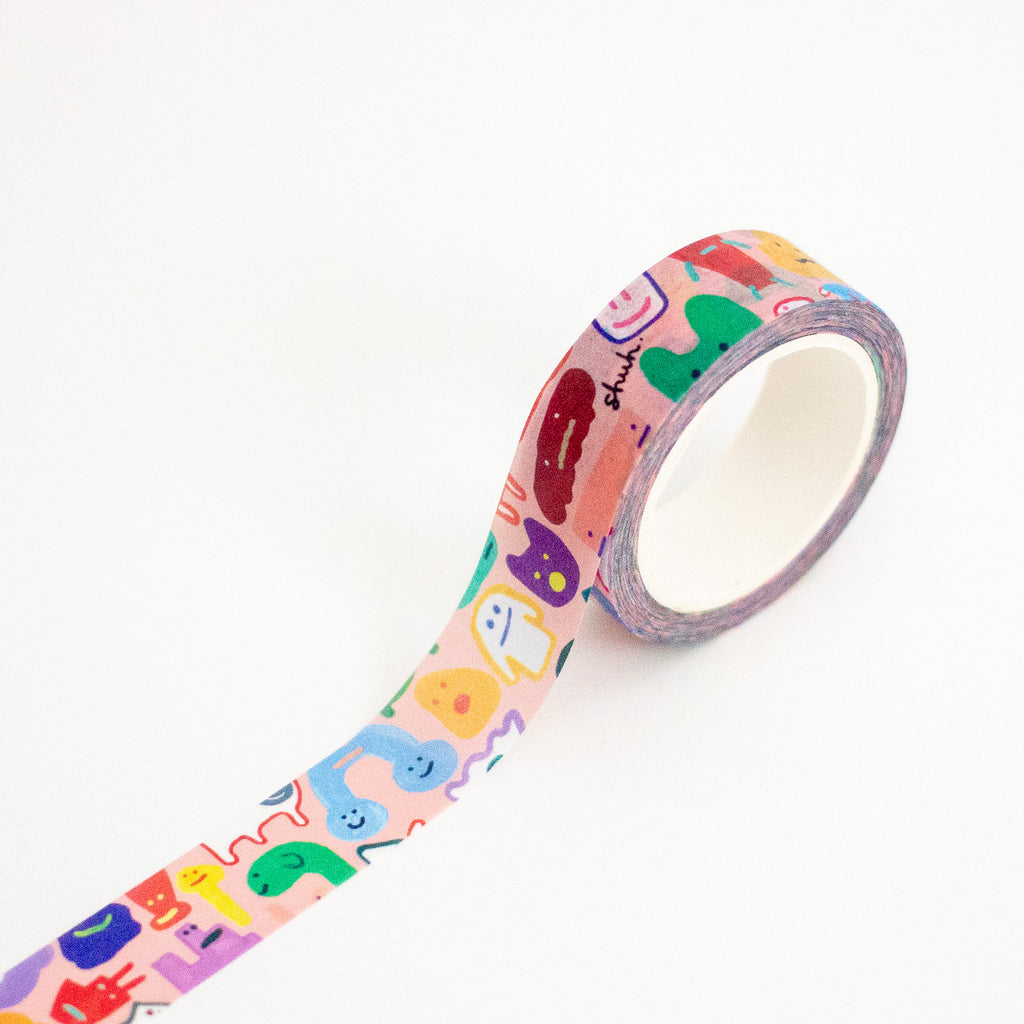 A roll of washi tape with a pastel multicolour cartoon monster pattern, shown partially unrolled on a clean white background.
