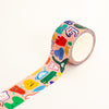 A roll of washi tape with a pastel pink background and colourful cartoon monster illustrations, shown with one end unrolled on a clean white background.