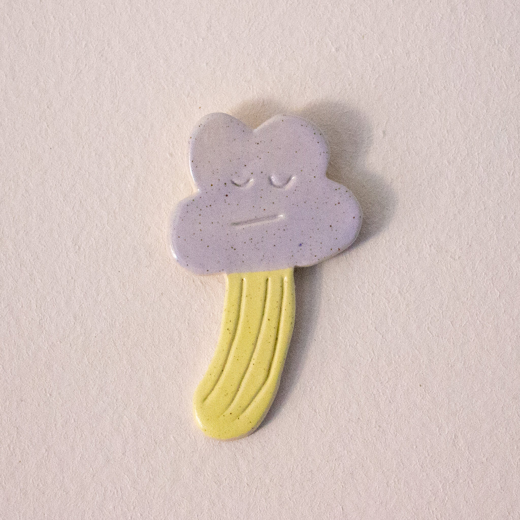 Solemn-looking cloud-shaped ceramic wall art with a yellow base on a light gray background