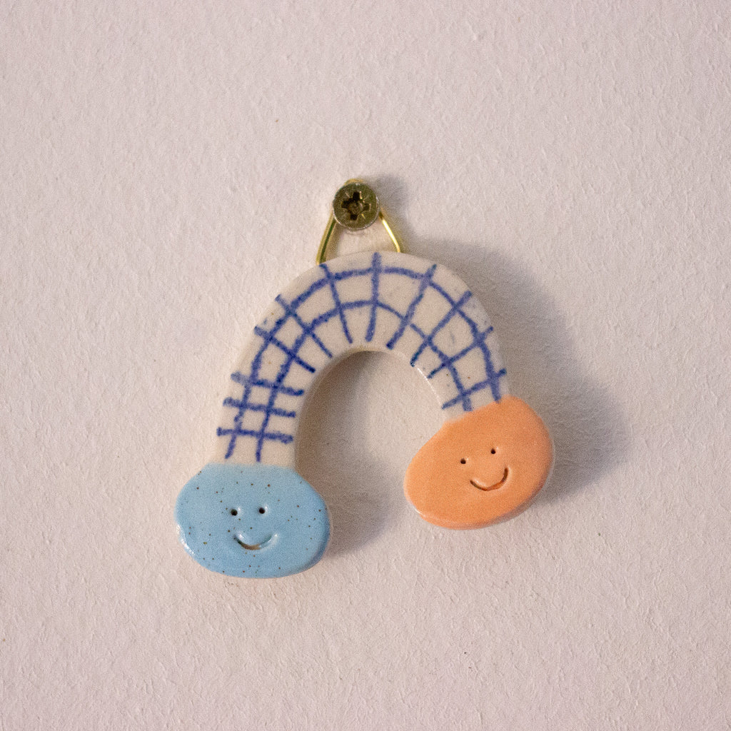 Decorative rainbow shaped ceramic wall art with a blue arch, orange circle, and blue circle on a beige background