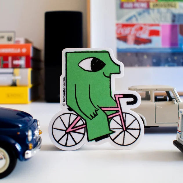 Green character on a bicycle sticker with toy cars in the background