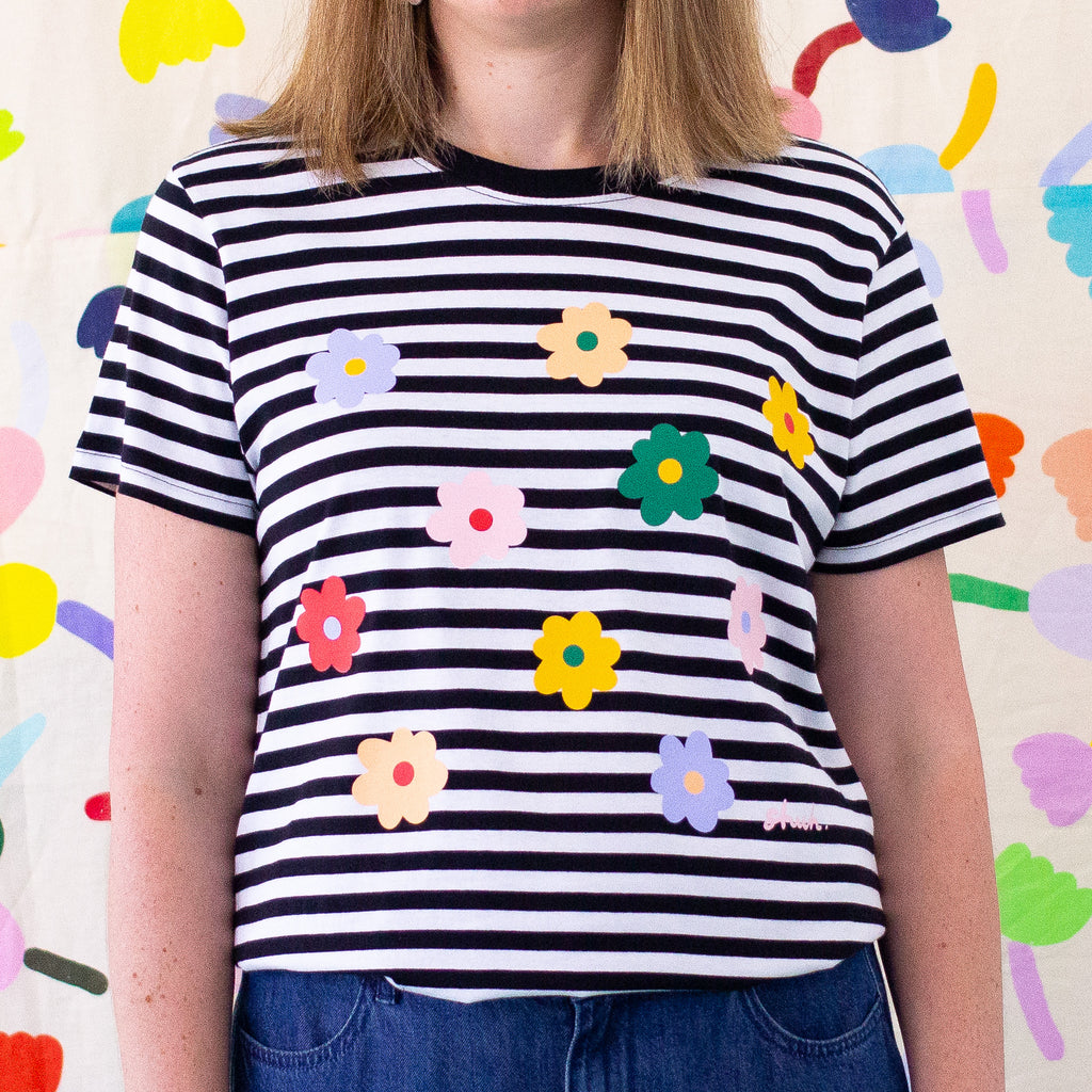 Front view of the Daisies tee. Black and white striped tee, with multicolour daisies printed on the front. 