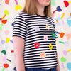 Side view of the Daisies tee. Black and white striped tee, with multicolour daisies printed on the front. 