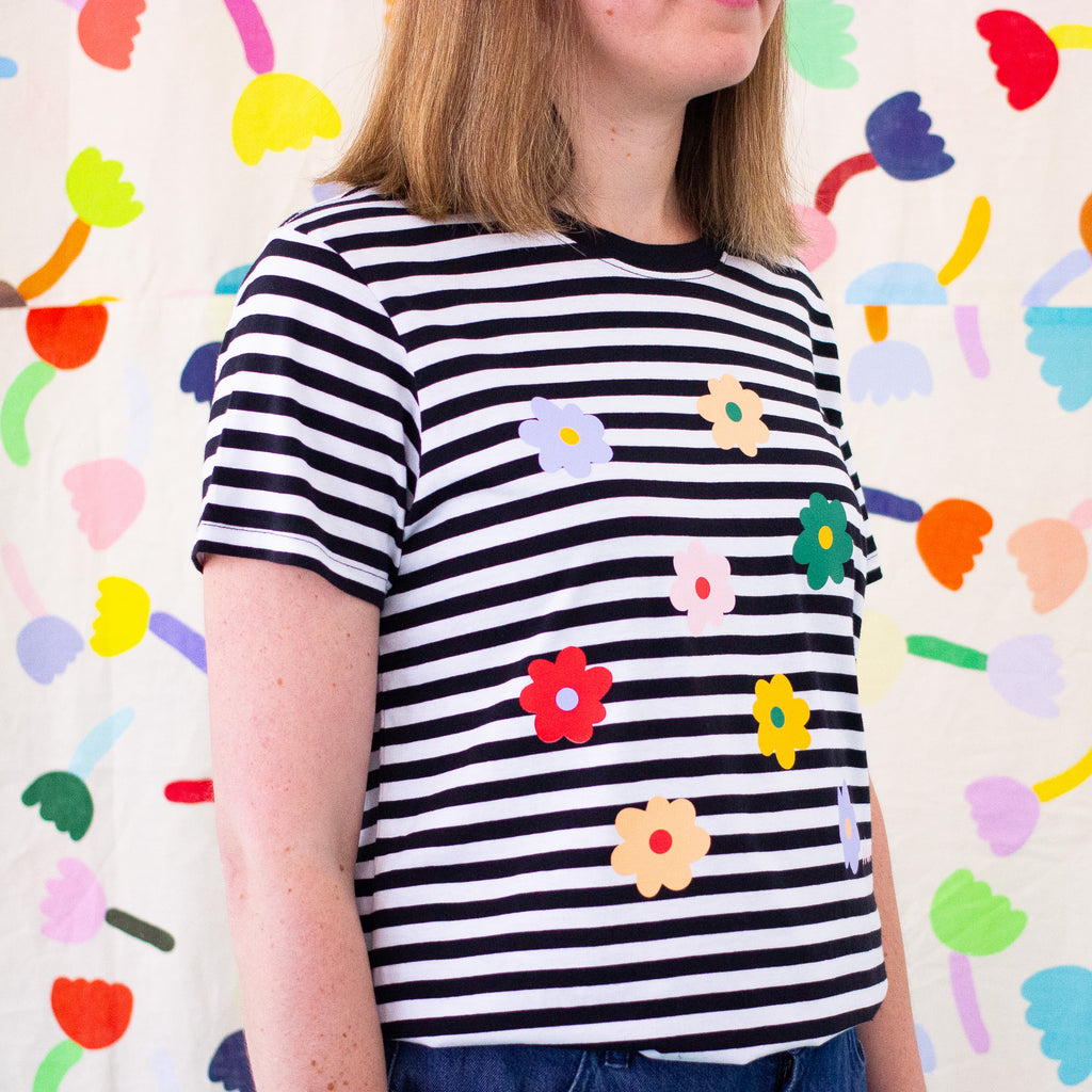 Side view of the Daisies tee. Black and white striped tee, with multicolour daisies printed on the front. 
