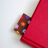 A colourful flower pattern bookmark,  shown peeking out of a closed book against a plain white background.