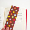A colourful flower pattern bookmark,  shown resting on an open book against a plain white background.