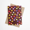 A card with colourful flower illustrations all over against a brown background with a shuh. logo on the bottom of the card on a kraft paper envelope. 