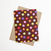 A card with colourful flower illustrations all over against a brown background on a kraft paper envelope. 