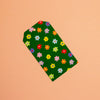 A green gift tag with a colourful floral pattern, photographed diagonally on a solid peach background.