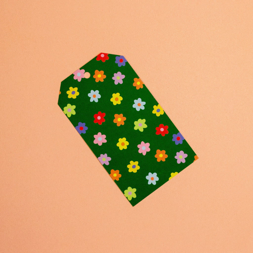 A green gift tag with a colourful floral pattern, photographed diagonally on a solid peach background.