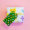A green gift tag with a colourful floral pattern attached to a yellow string on a gift box.