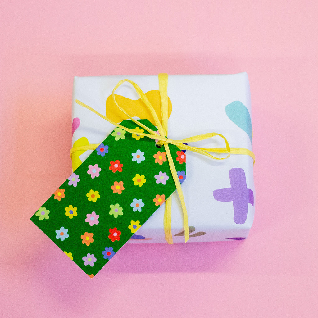 A green gift tag with a colourful floral pattern attached to a yellow string on a gift box.