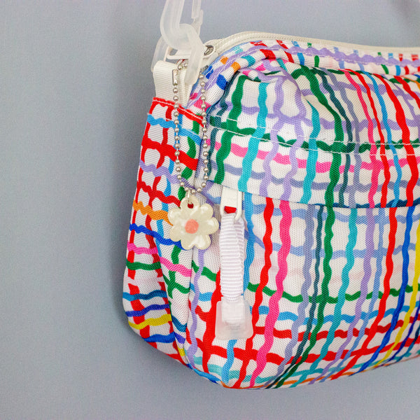 Colourful patterned pouch with a white flower charm on a grey background