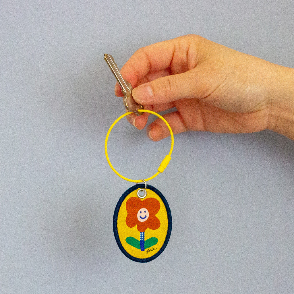 Hand holding a key with a colourful keychain featuring a flower design on a grey background
