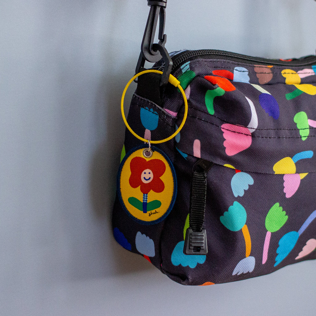 Colourful patterned bag with a keychain featuring a smiling flower design on a plain background