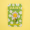 A daisy-shaped enamel pin with a smiling yellow face, white petals, and green leaves, mounted on a green floral backing card that reads 'DAISY Pin By Hannakin'.