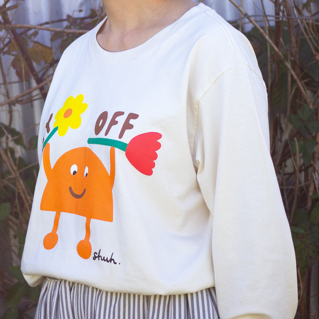 Side view of a Person wearing a beige long sleeve t-shirt with a colourful graphic of an orange cartoon character holding two flowers and the words "DAY OFF" in playful text. Design by shuh., printed in Australia.