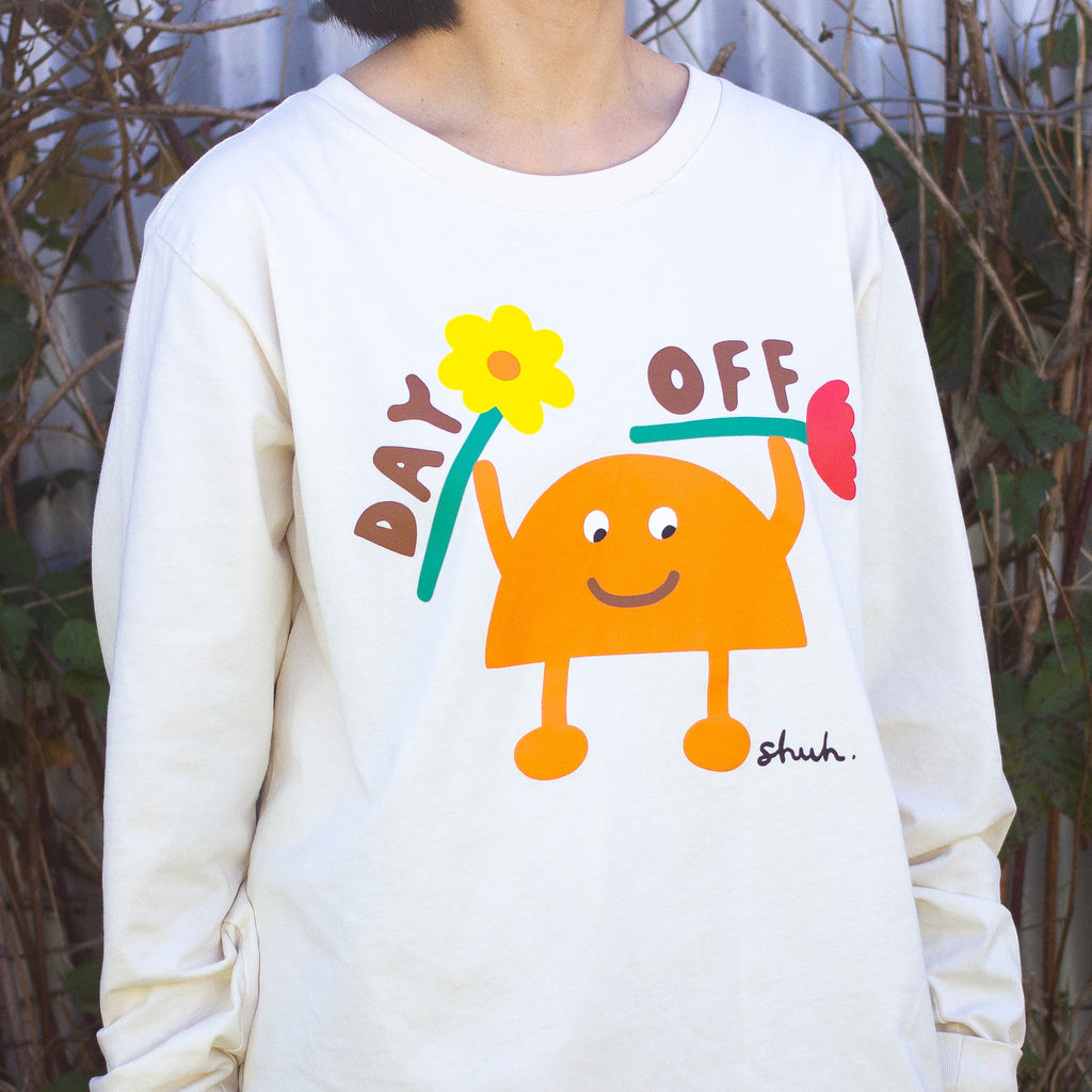 Person wearing a beige long sleeve t-shirt with a colourful graphic of an orange cartoon character holding two flowers and the words "DAY OFF" in playful text. Design by shuh., printed in Australia.