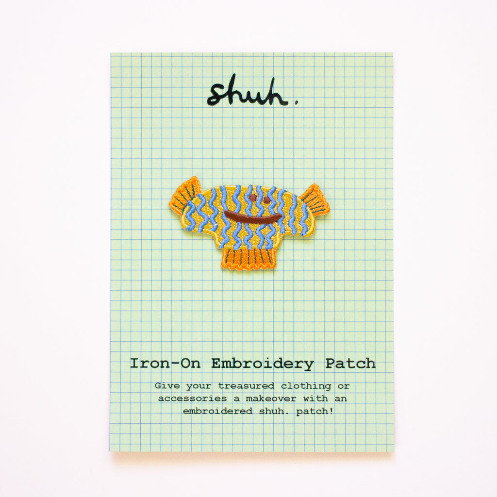 Iron-on embroidery patch of a fish with a colorful pattern on a checkered card.