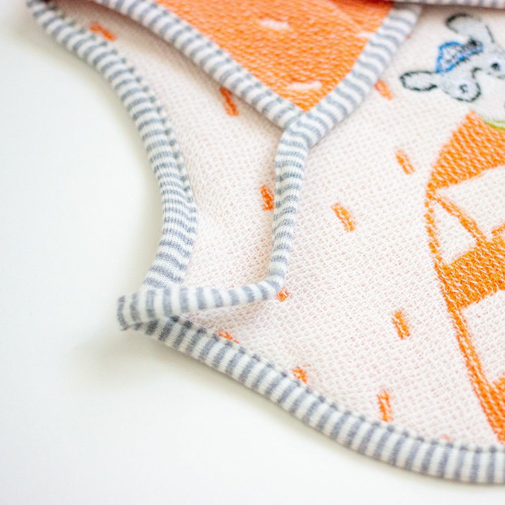 Close-up of a baby bib with a white base, orange pattern, and grey-and-white striped trim, photographed on a white background.