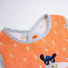 Close-up of a knitted baby bib in bright orange with a grey and white striped binding and a small cartoon animal face.