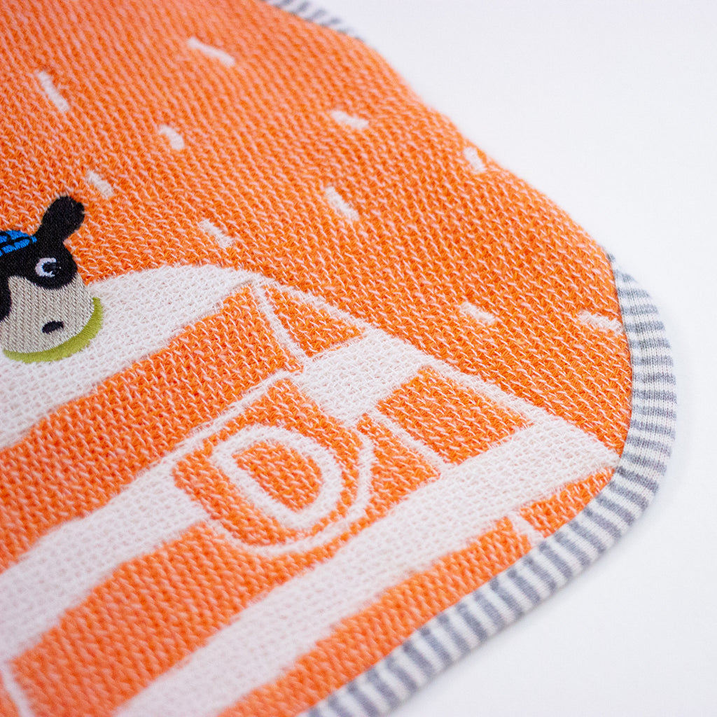 Close-up of a textured orange and white fabric item with a cartoon dog graphic and striped grey trim on a white background.