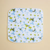A square handkerchief with rounded corners, featuring a white background printed with a pattern of light blue flowers, white blossoms, and olive green leaves. The cloth has a white merrowed border and is photographed flat against a solid beige background.