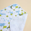 A close-up of a soft white fabric item, featuring a light blue and olive green floral pattern on one side and a plain white textured reverse side, set against a solid beige background.