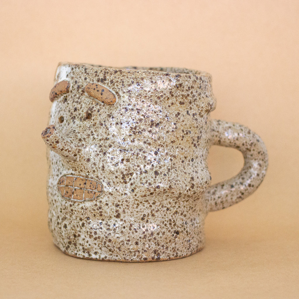 Closeup of the doink figurine, with more focus on the side. A large mug shaped sculptural piece made of stoneware clay with natural glaze. Features mouth, eyes, and nose, all hand carved into the figurine. 