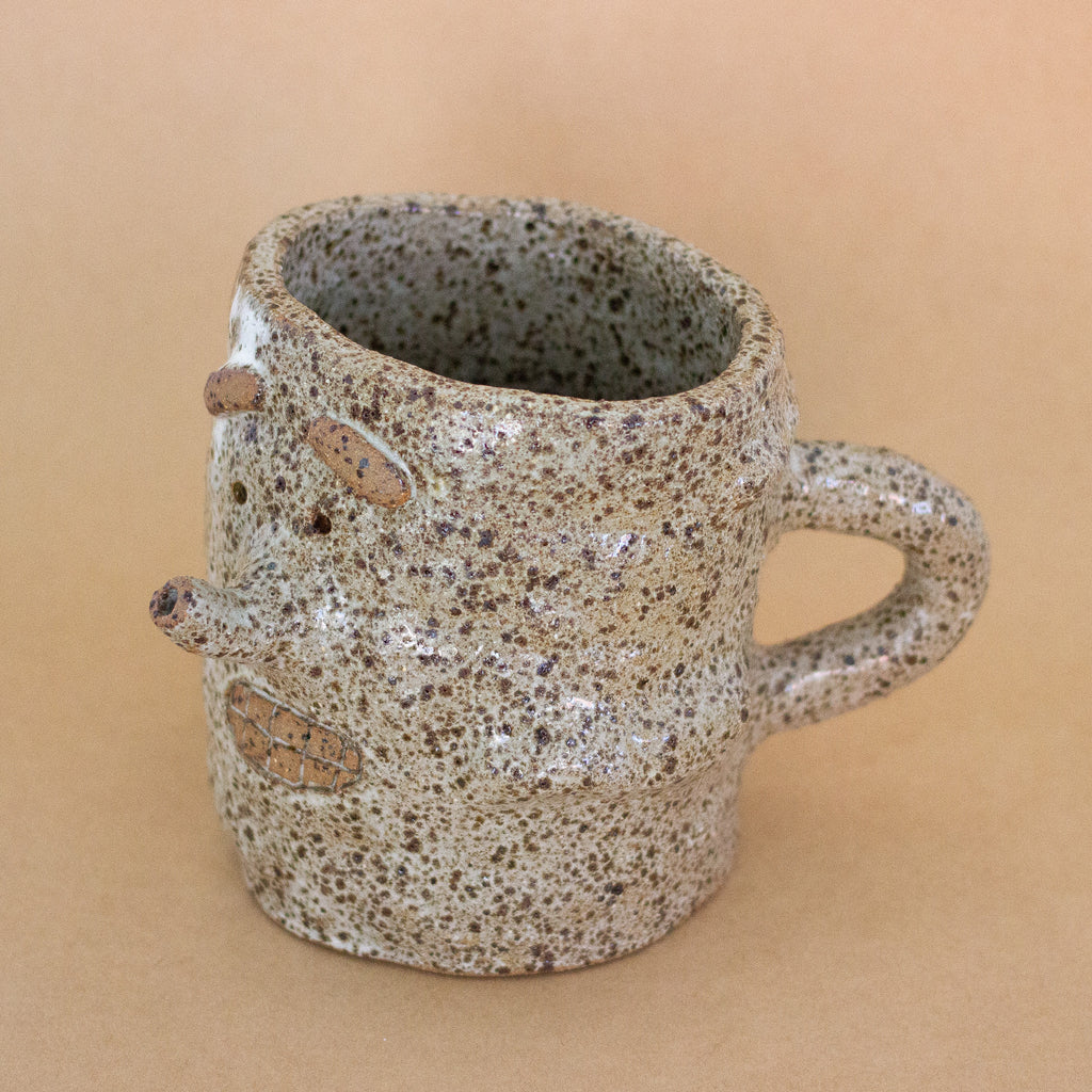 Closeup of the doink figurine, with focus on the top opening. A large mug shaped sculptural piece made of stoneware clay with natural glaze. Features mouth, eyes, and nose, all hand carved into the figurine. 